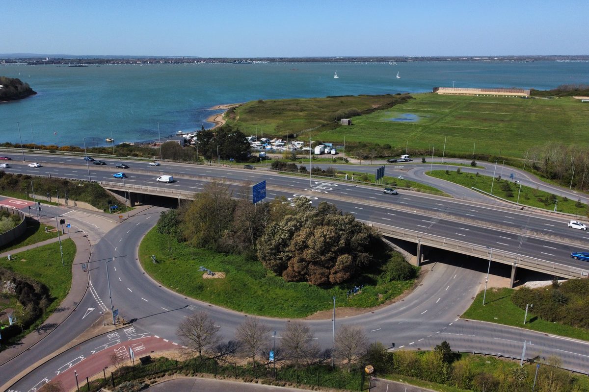 Aerial view of the M275 flyover and Tipner roundabout, with Portsmouth Harbour and sailing boats beyond