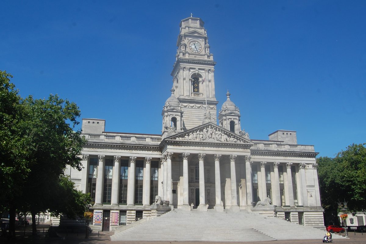 Portsmouth Guildhall, a white stone building with columns, wide steps and a clock tower, under a clear blue sky